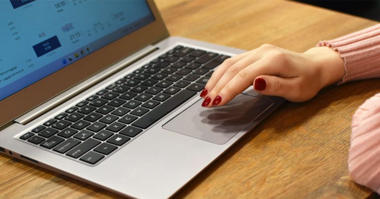 A woman with red nail polish types on a laptop on top of a wooden desk in an alternative to nanowrimo.