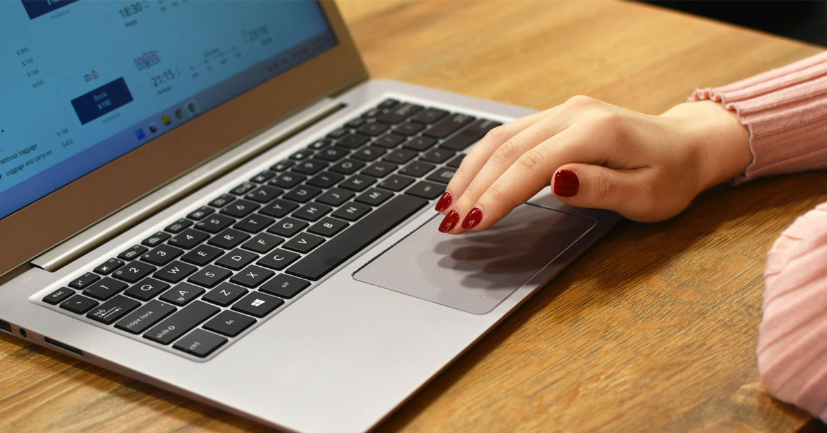 A woman with red nail polish types on a laptop on top of a wooden desk in an alternative to nanowrimo.