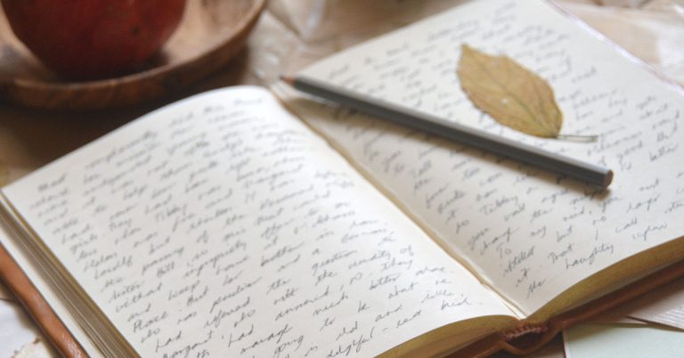 A journal filled with handwriting lays on a desk topped with a grey pencil.