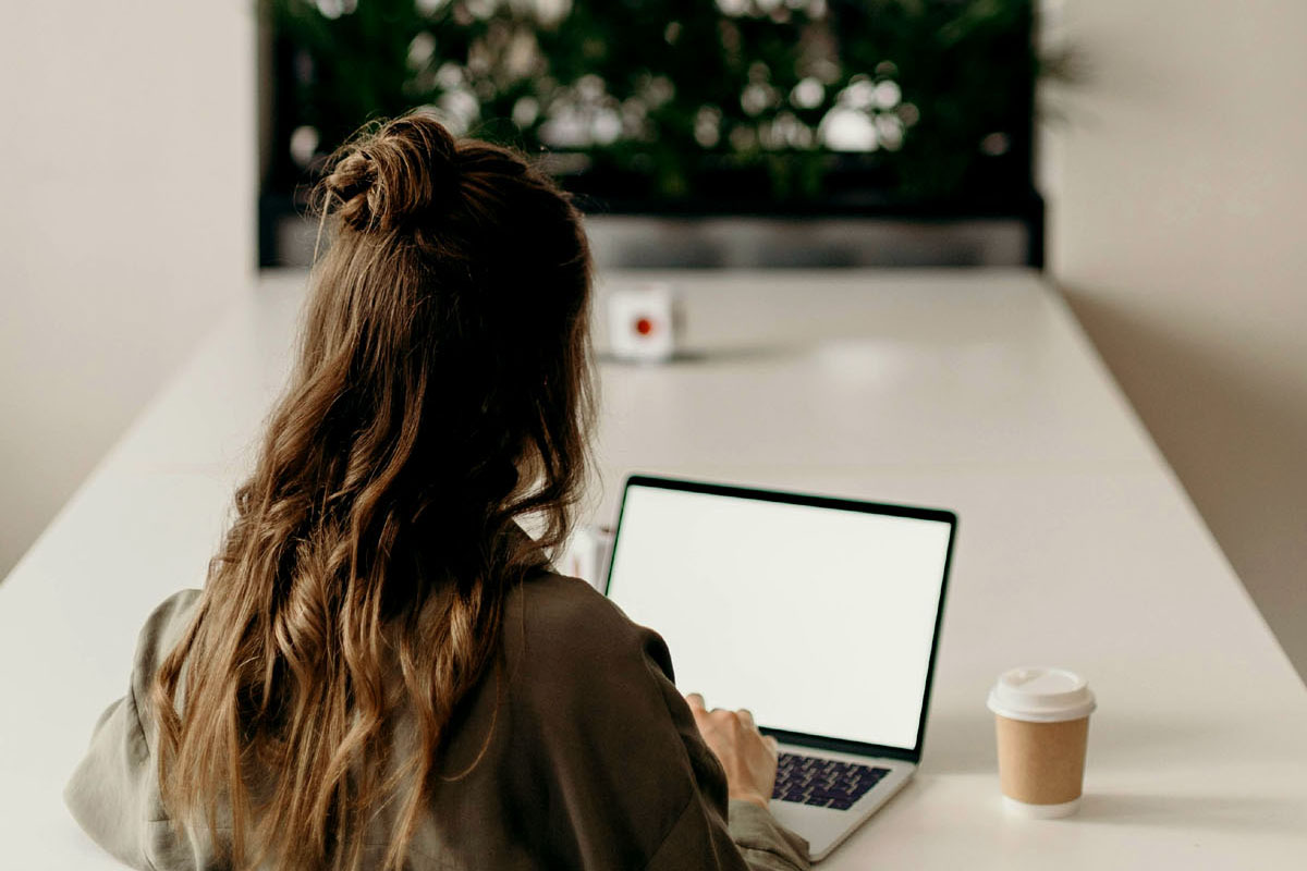 A woman sits in front of a laptop at a large desk.