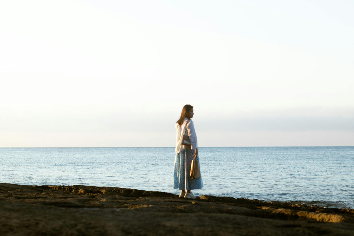 A woman stands on the shore looking out over the water.