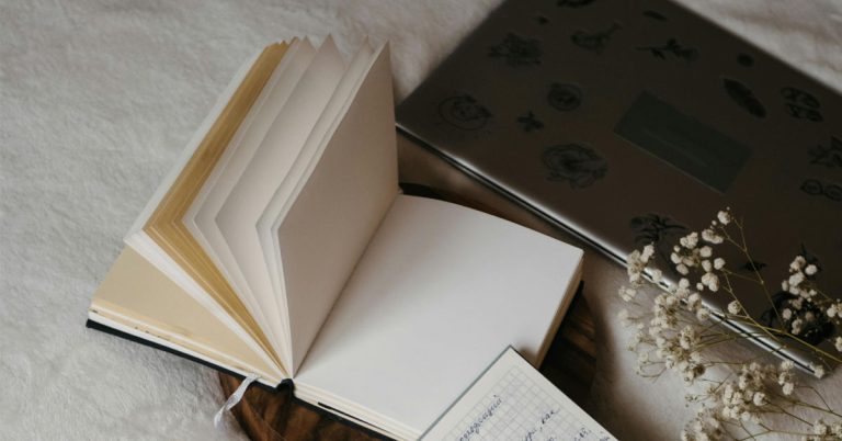 A blank journal lays open filled with depression journal prompts on top of a bed beside a darker journal.