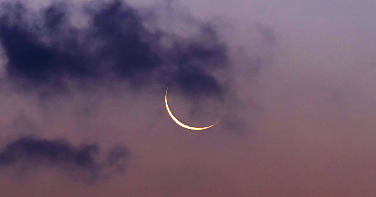 A new moon with a thin crescent shines through the crowds against a rosy sky.