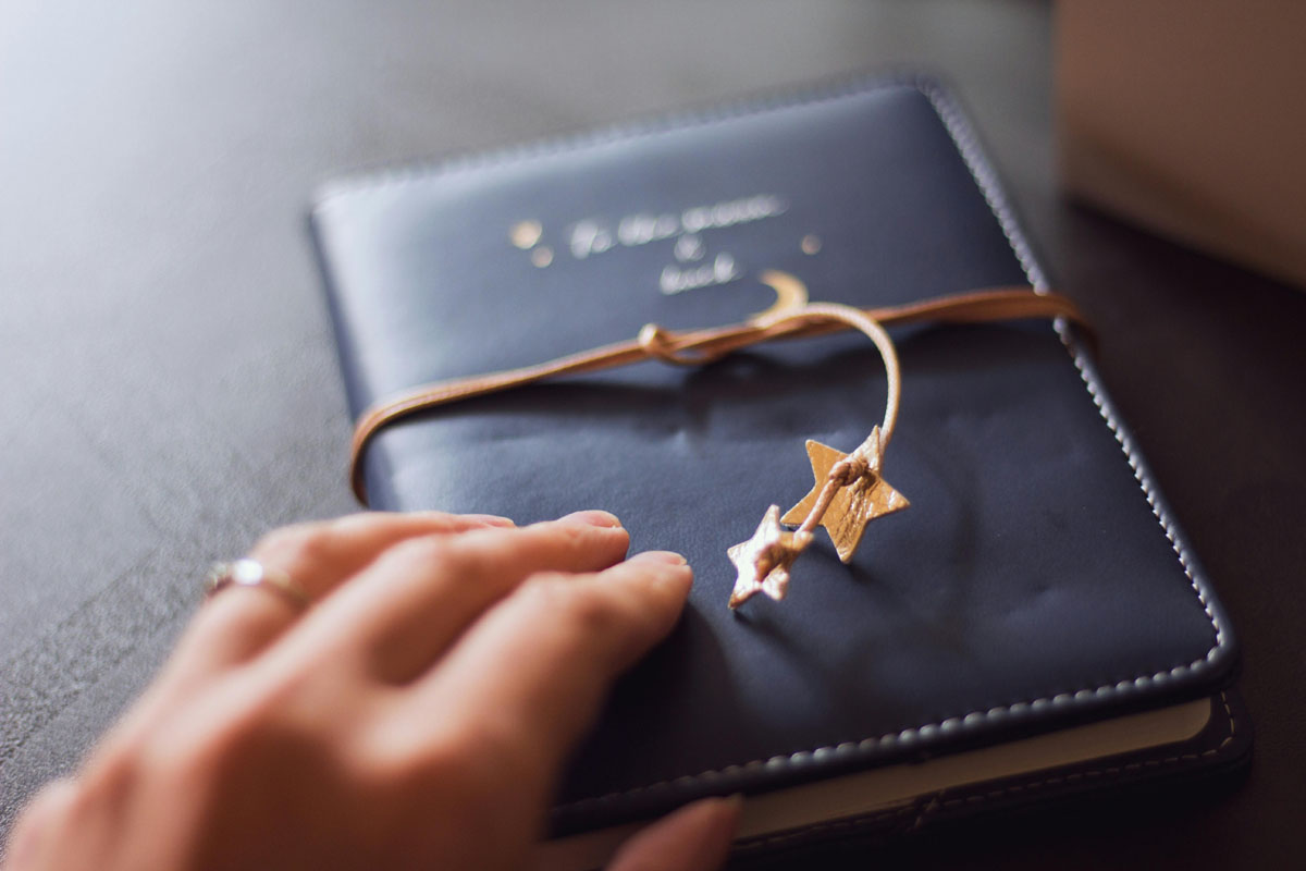 A hand reaches out for dark leather journal tied with wooden stars.
