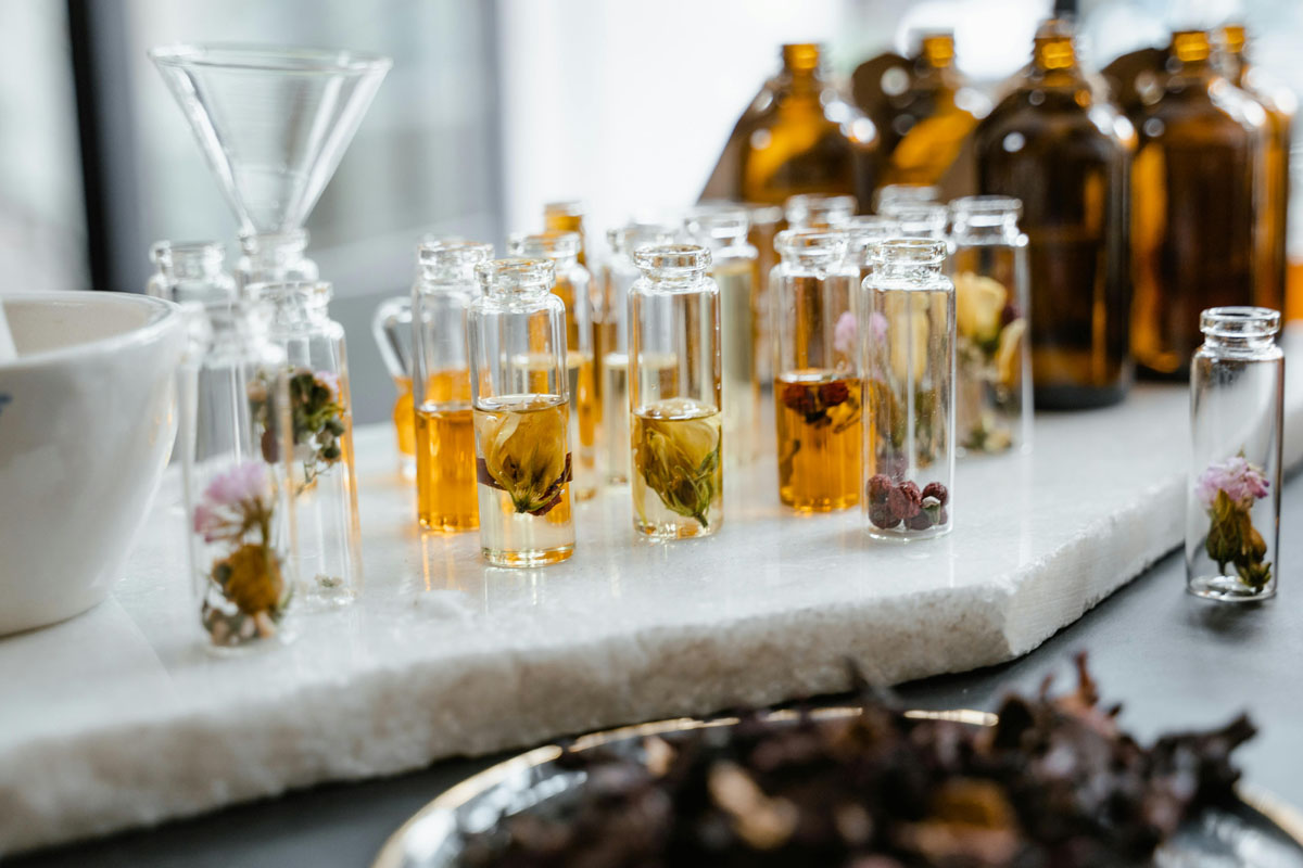A selection of tiny bottles filled with flowers, herbs and oils sands on a marble counter.