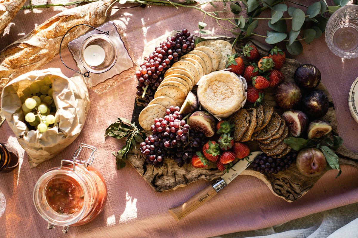 Fruits, crackers and cheeses lay in the sun on a peach throw.