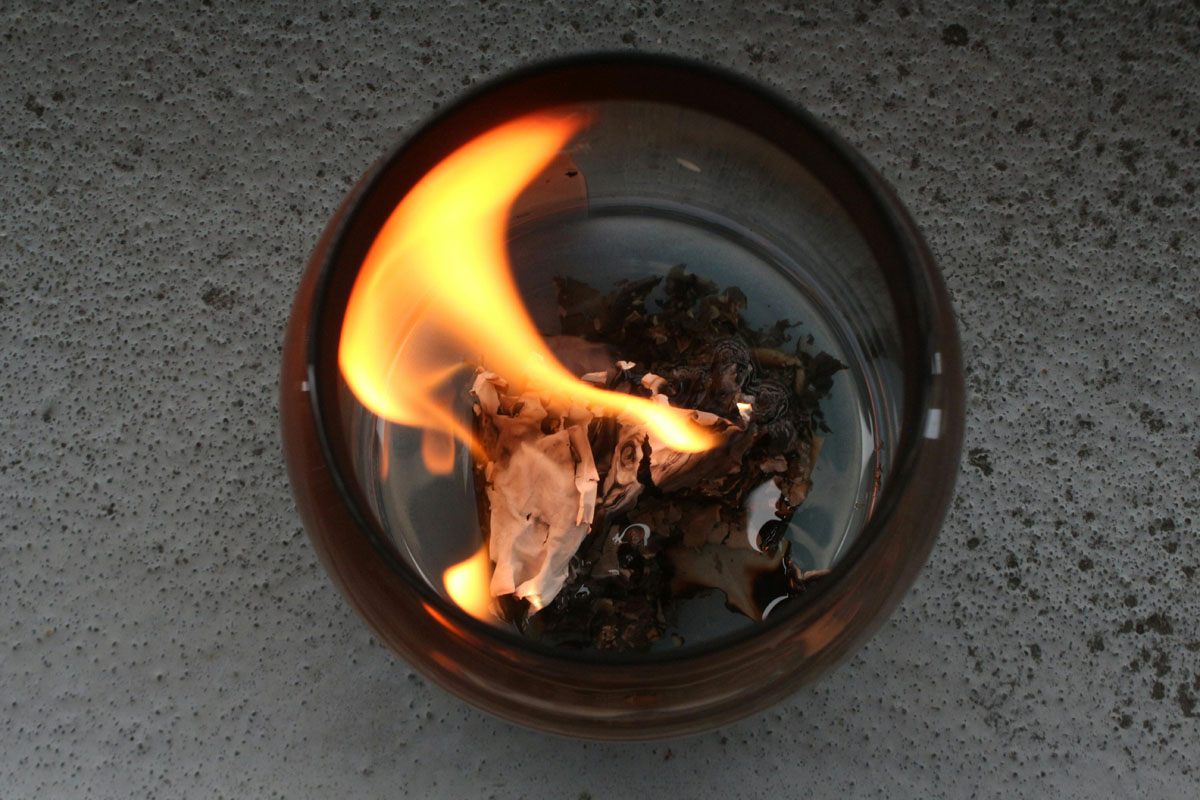 A bowl on a grey table with burning paper inside as an example of a summer solstice celebration.