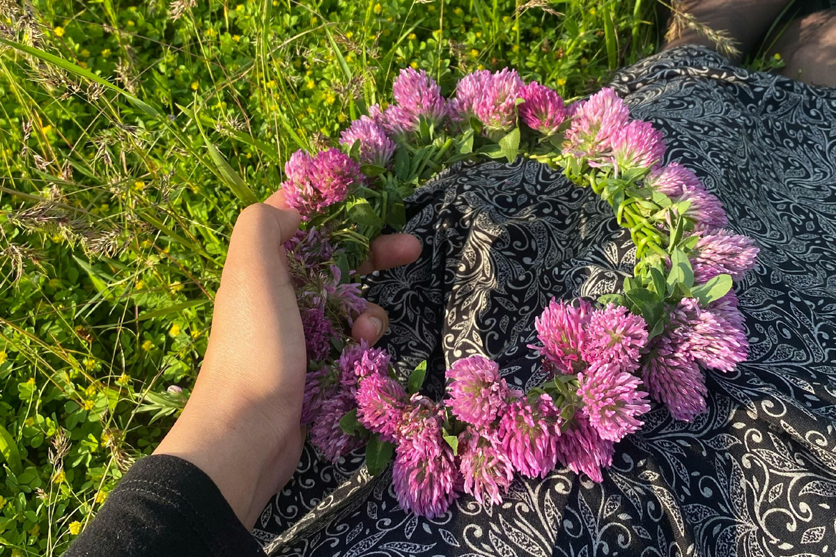 A woman holds a purple flower crown as she sits in the grass.
