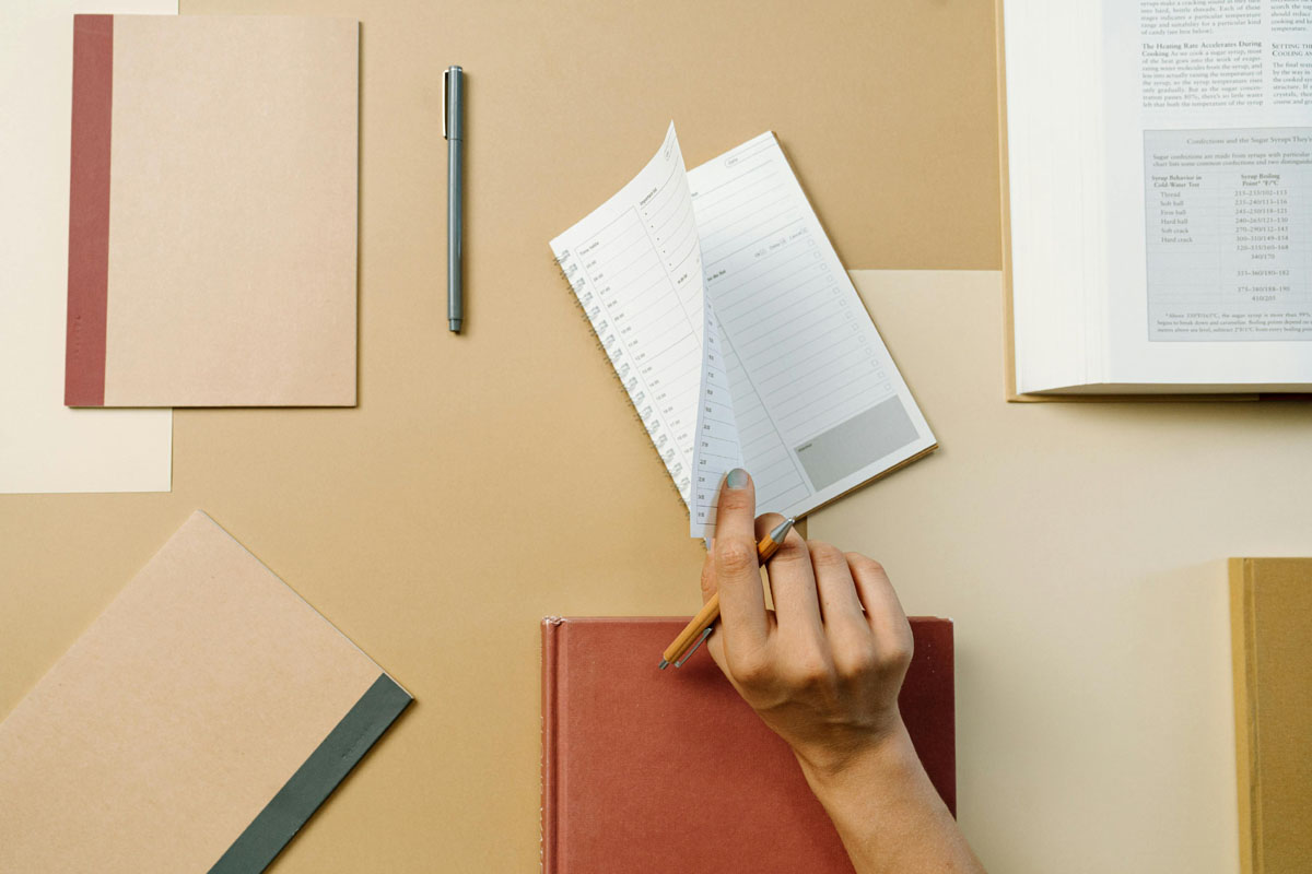 A hand opens a bullet journal laying on an ochre desk.