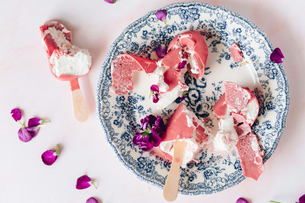 A blue china plate lays on a white counter with pink ice cream and flower petals inside.