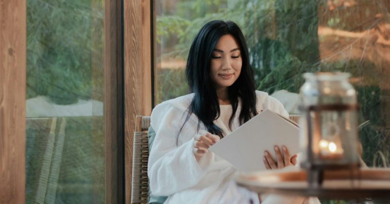 A woman sits at a table surrounded by greenery flipping through a large notebook of dopamine menu ideas.