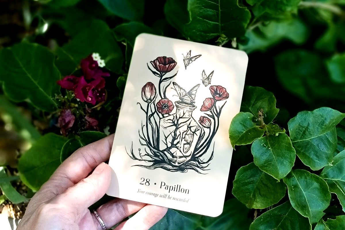 Dee holds up an oracle card showing flowers against a background of greenery.
