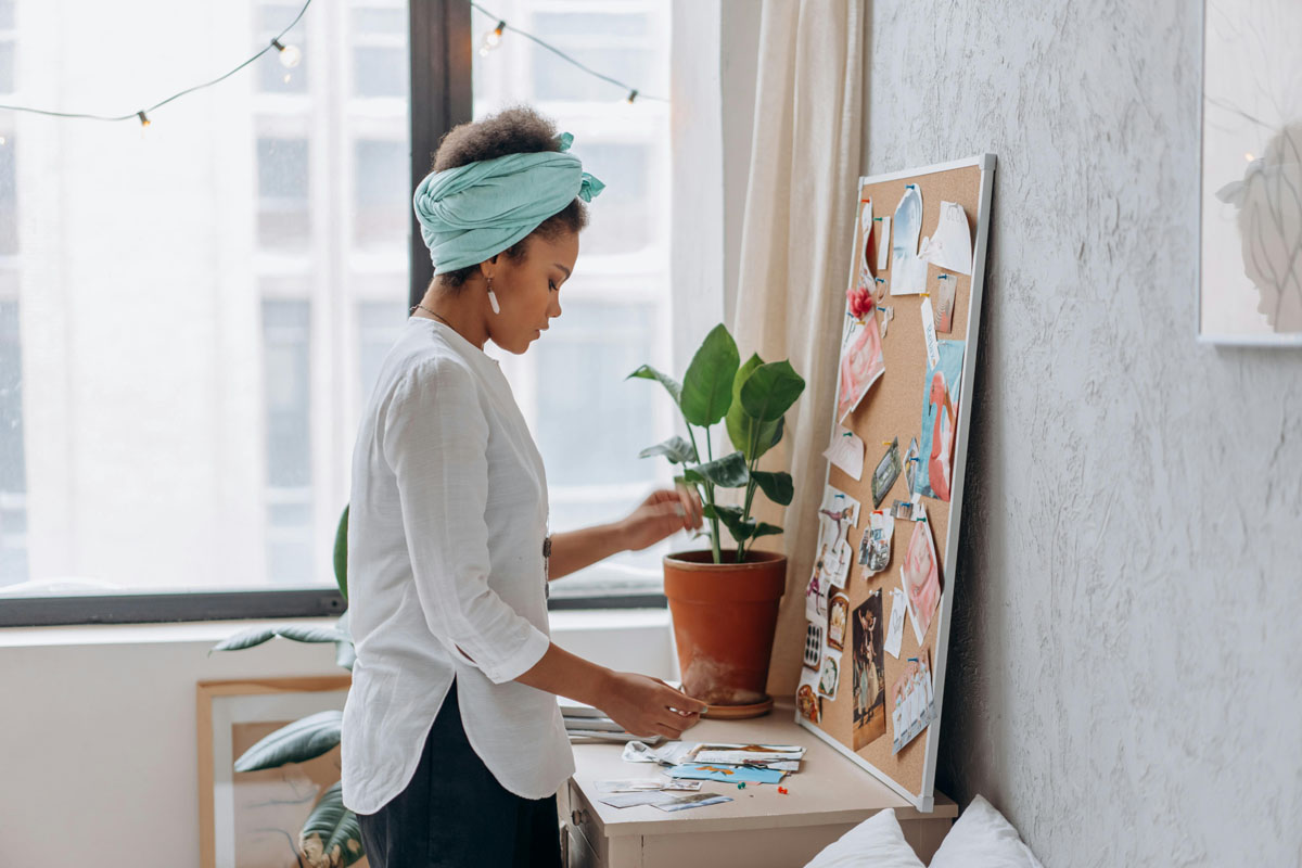 A woman in a blue turban and white shirt stands in front of a vision board selecting images.