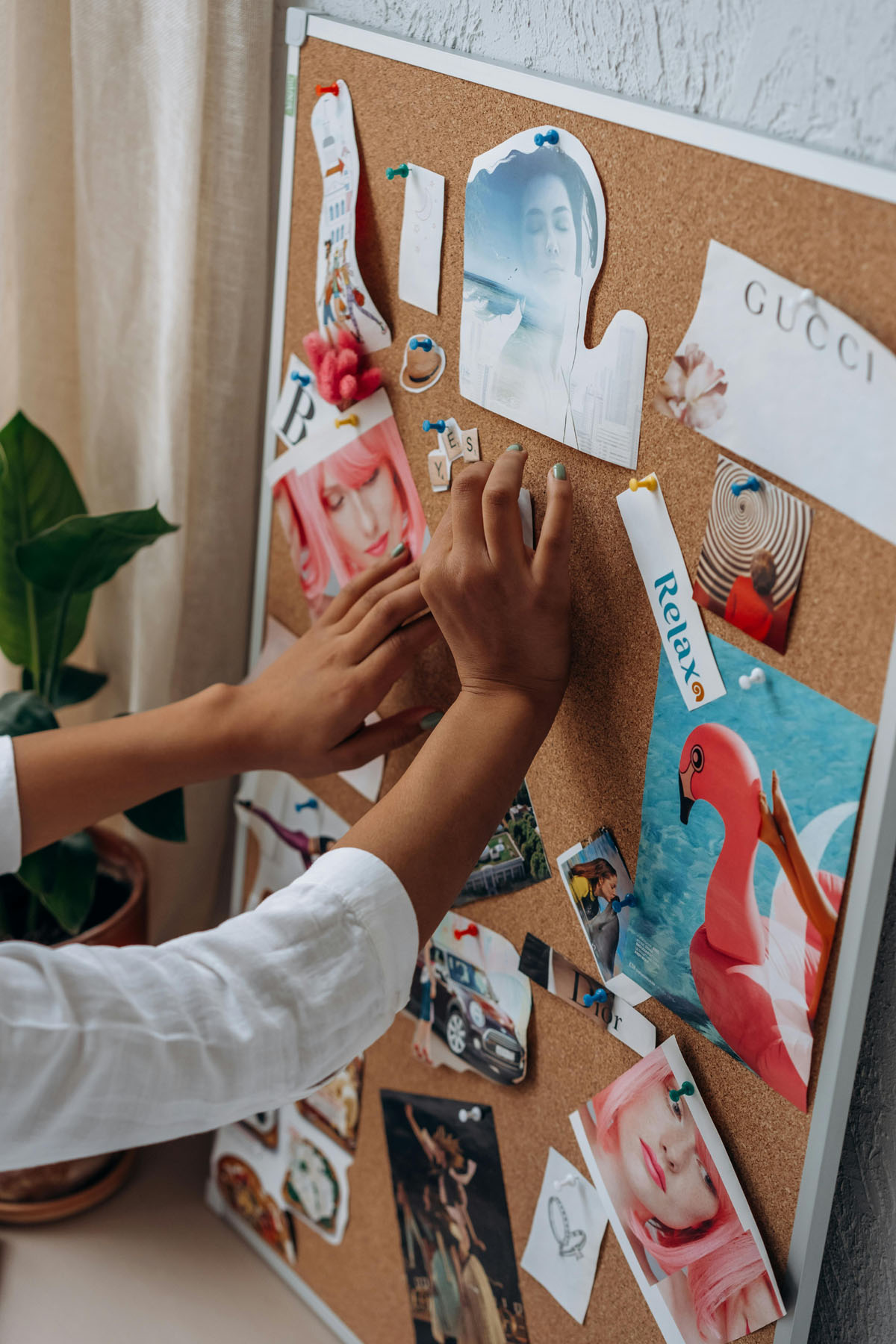 Hands on a bulleting board pin up colorful images onto a vision board.