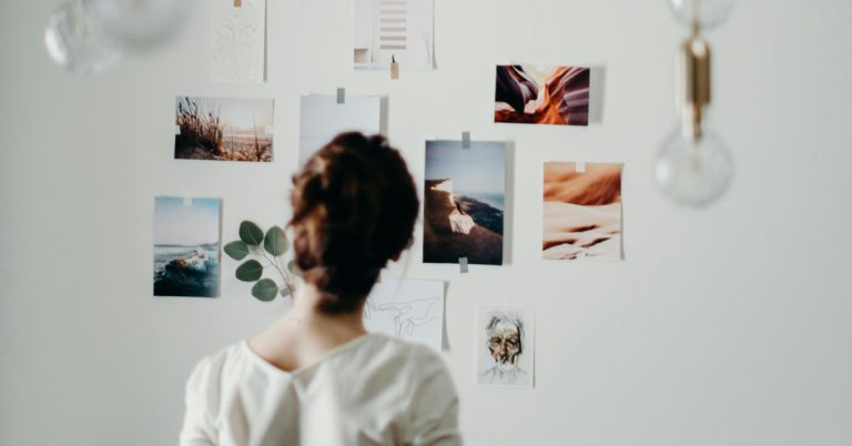 A woman in white looks at a white wall filled with magazine clippings and images full of vision board ideas.
