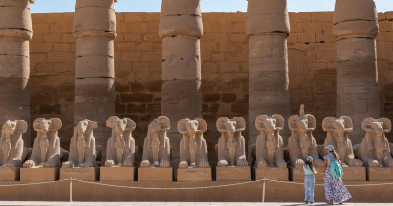 A mother and daughter gaze out over a row of ancient Egyptian statues in Luxor.