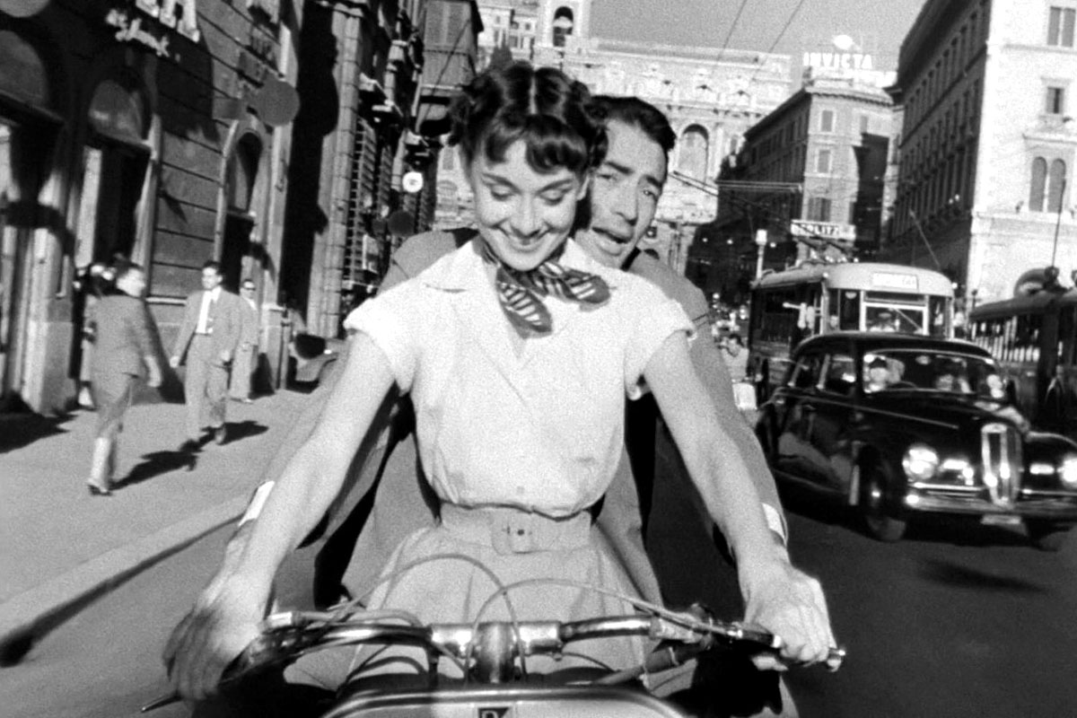 An image from the movie Roman Holiday with Audrey Hepburn riding a scooter with a panicked man in the back.