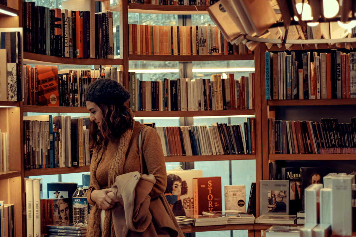 A woman walks through shelves of books inside a book store.
