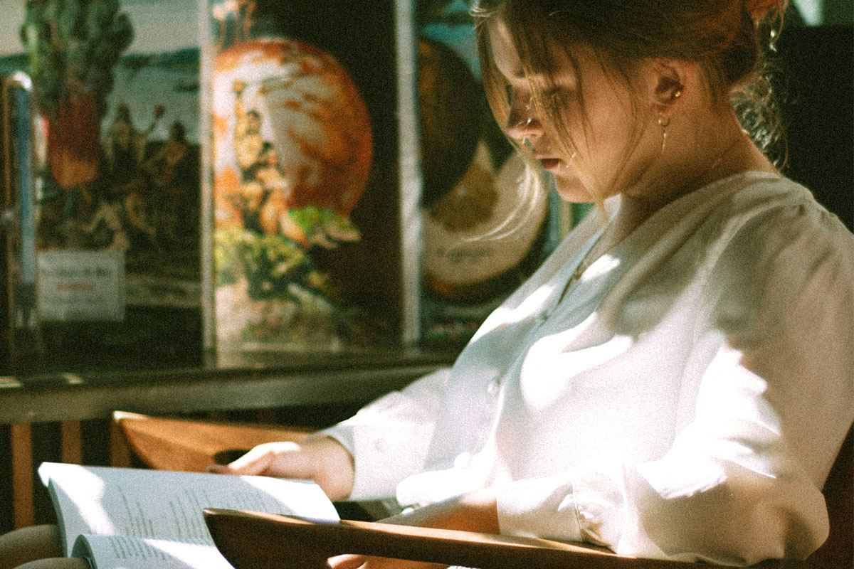 A woman wearing white sits reading at a local library.