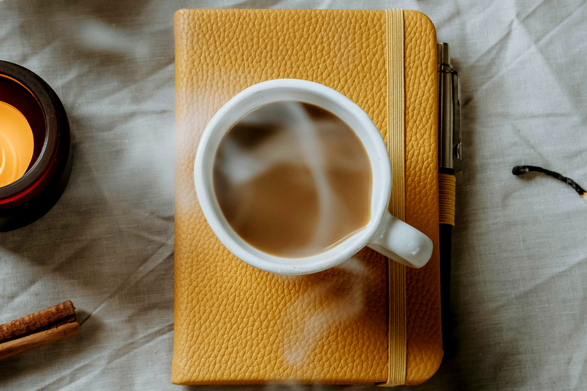 A steaming cup of tea lays on top of a bright yellow notebook.