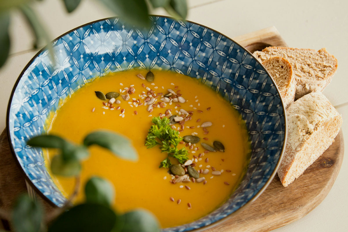 A bowl of yellow vegetable soup lays on a table in a blue bowl.