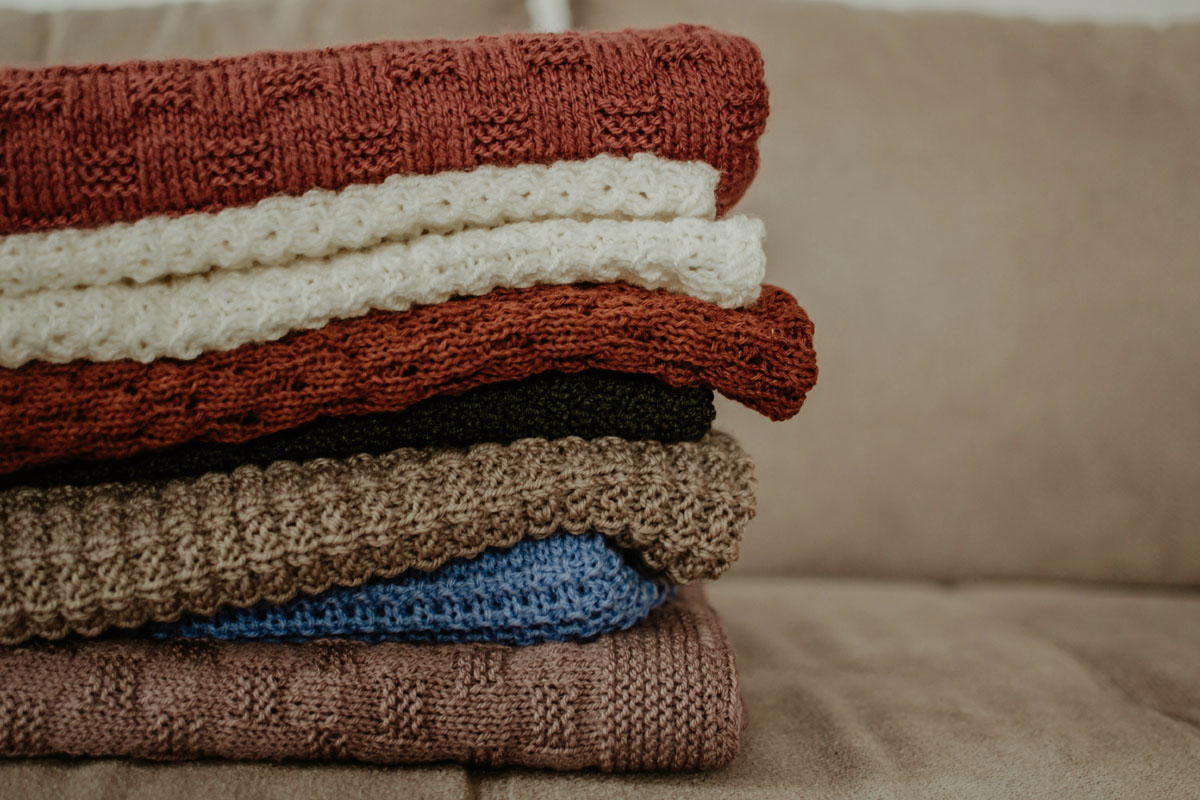 A pile of sweaters lays on a bed in an example of a decluttering session during a September reset. 