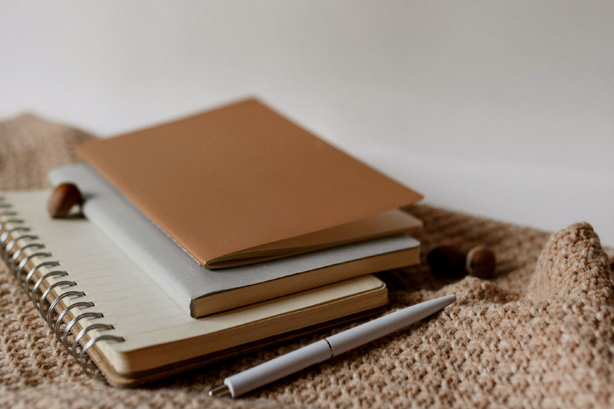 A pile of gratitude journals lay on a bed alongside a silver pen.