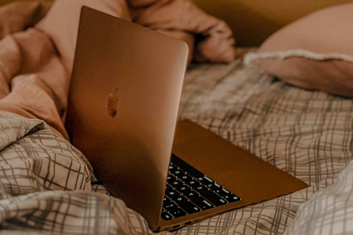 An open laptop lays on a checkered bed comforter. 