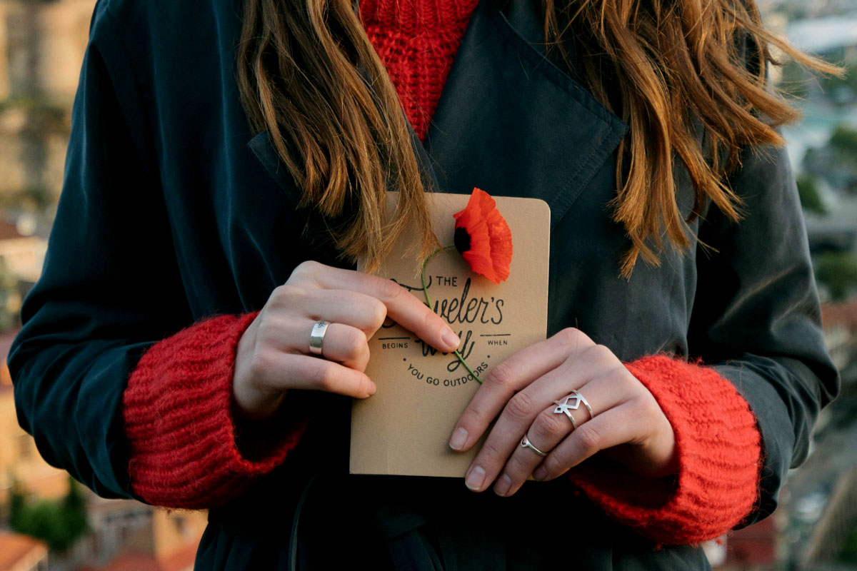 A woman in a red sweater and dark coat holds a beige travel journal.