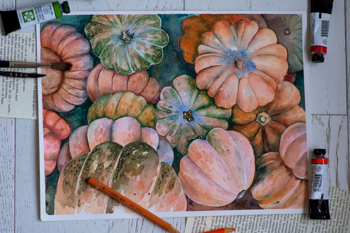 A watercolor sketch of pumpkins lays on a table alongside tubes of paint.
