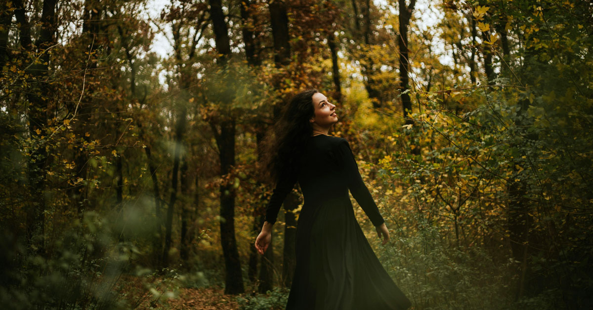 A woman flips her hair back while walking through a forest in an example of the feeling of a September reset.