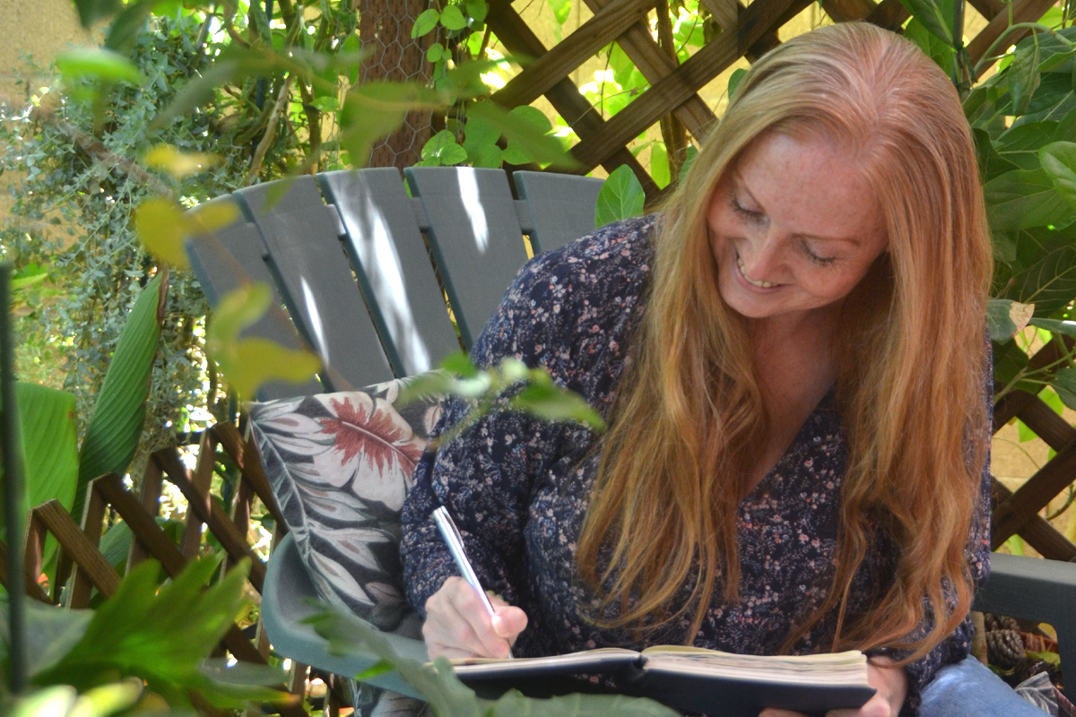 Dee sits in the garden writing in her journal.