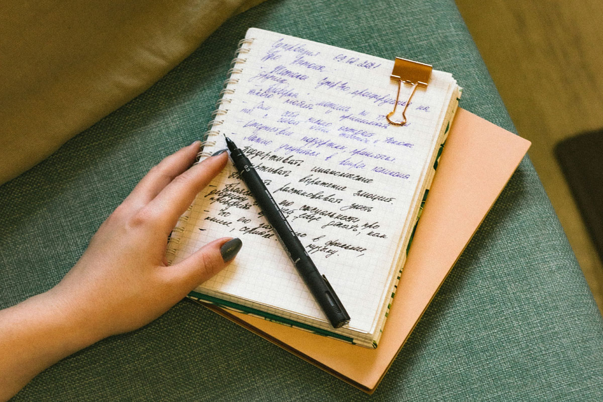 A close-up of a hand resting on a stack of handwritten paper journals used for mental health and reflection.