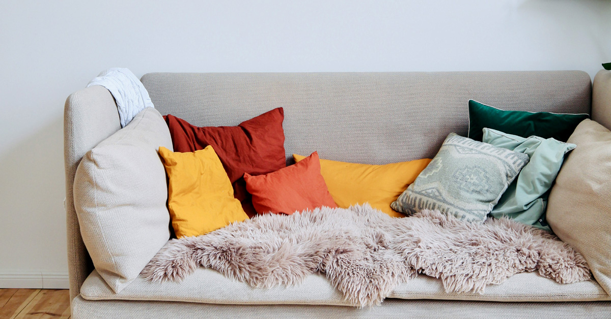 A minimalist couch stands against a grey wall with colorful cushions.