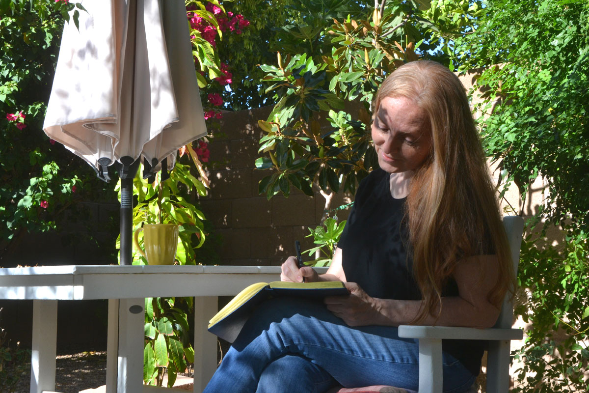 Dee writing in her journal in a sunny garden.
