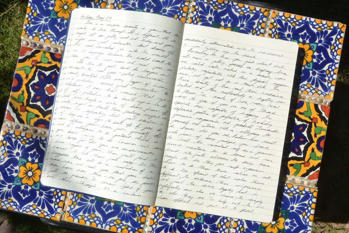 A paper journal lays in the sun on a table of Spanish tiles.