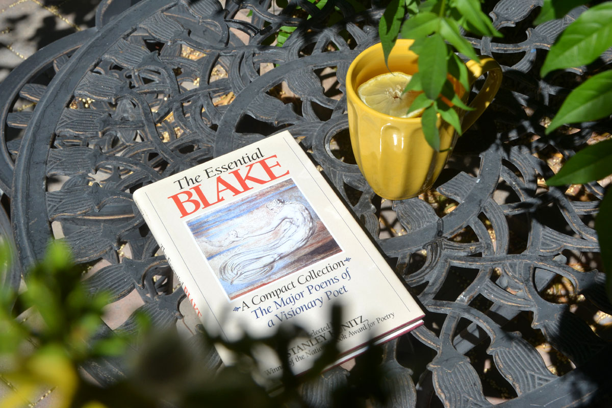 A book of William Blake poetry lays on a patio table next to a yellow mug of tea.