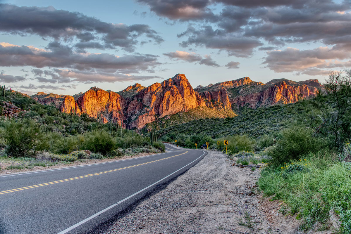 A highway in Arizona with some sunlit mountains in the distance.