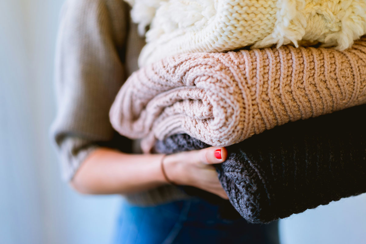 A woman holds a pile of laundry in an example of a task on a sunday reset checklist. 
