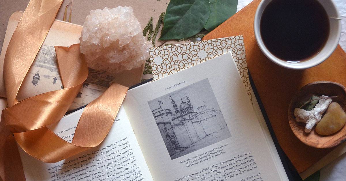 An open book lays on a table next to a cup of coffee and ribbons as an example of digital detox activities.