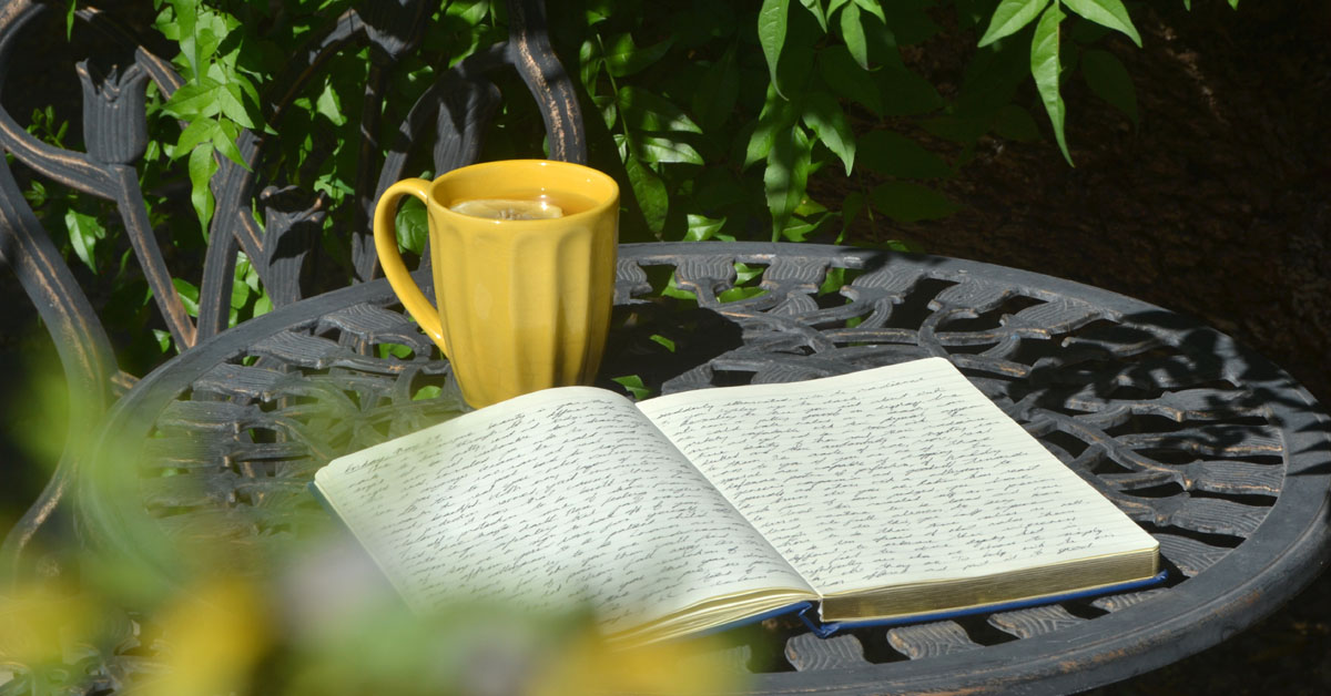 A journal lays on a garden table next to a yellow mug.