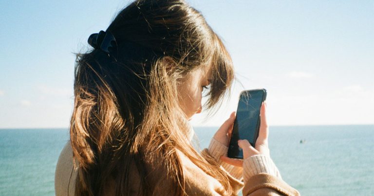 A woman scrolls on her phone on the beach..