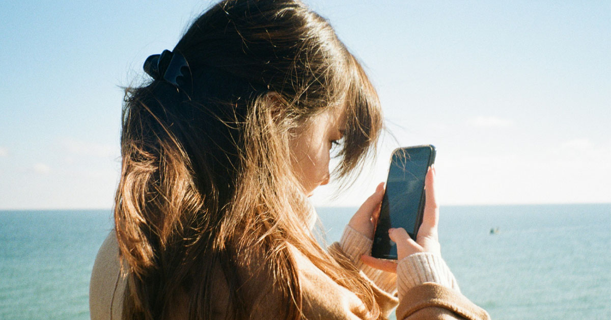 A woman scrolls on her phone on the beach..