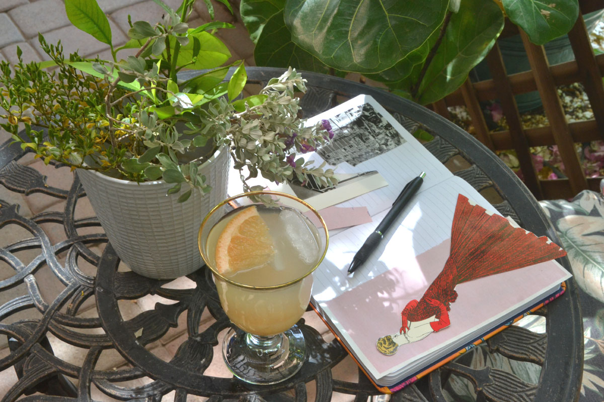A journal full of collage work lays open on a garden patio table.