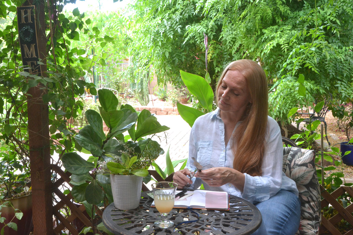 Dee sits in a garden surrounded by greenery doing some creative journaling with collage.