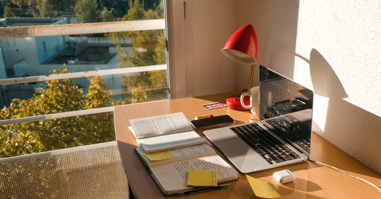 A desk with a decluttered inbox that includes a laptop, lamp and notes.