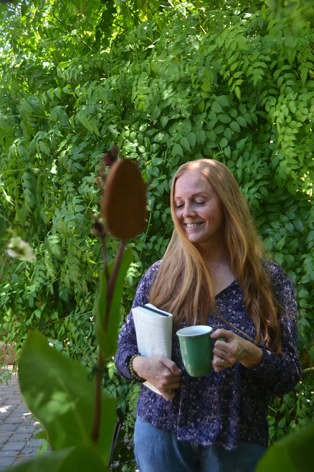 Dee stands in the garden with her journal and a cup of coffee.