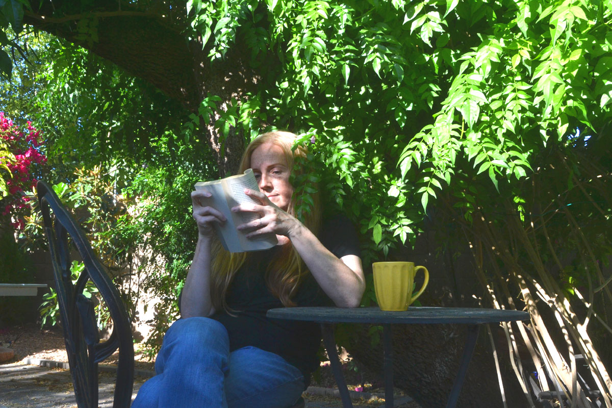 Dee sits in the garden reading a novel.