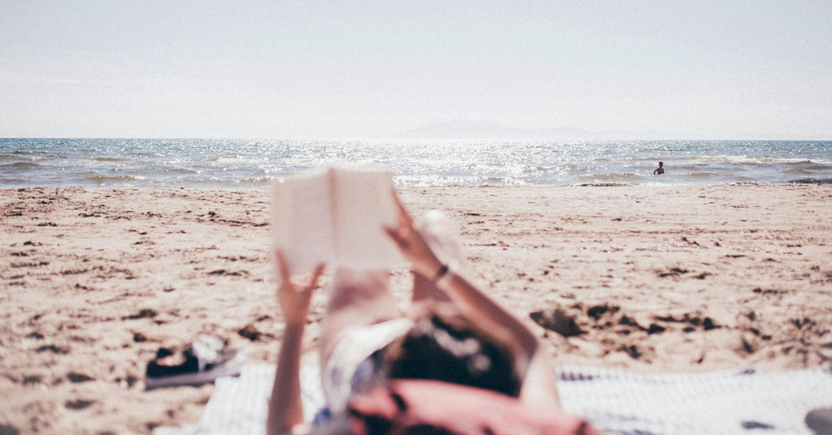 A woman lays on the beach reading a Nora Roberts novel.