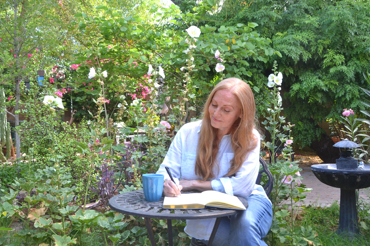 Dee sits in a garden writing in her journal. 